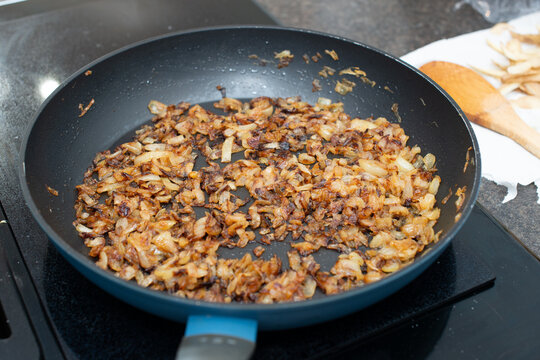 A large black colored iron frying pan full of sweet white onions minced and chopped into being fried or sauteed in butter. The edges of the diced onion have browned and caramelized to sweeten. 