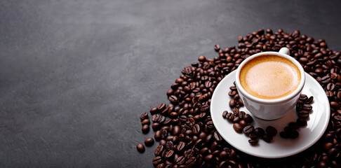 Horizontal banner with cup of coffee and coffee beans on dark stone background. Top view. Copy...