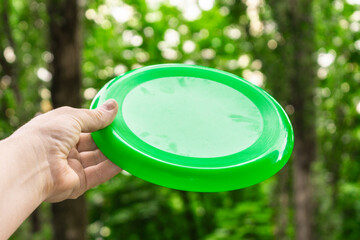 A hand with a disc for playing frisbee on the background of the park. The concept of mobile games.
