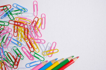 Colored pencils and paper clips white background, school supplies and stationery.