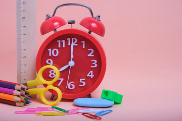 Red alarm clock,school supplies and stationery on a pink background.