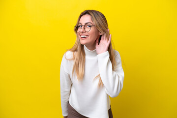 Young Uruguayan woman isolated on yellow background listening to something by putting hand on the ear - obrazy, fototapety, plakaty