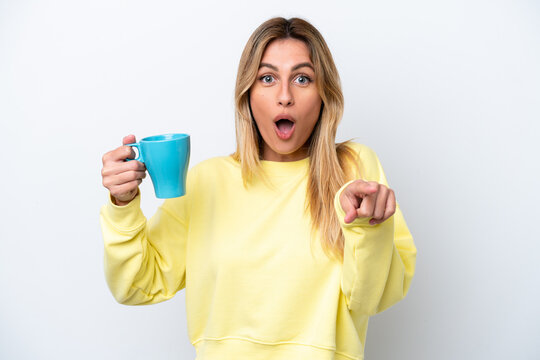 Young Uruguayan woman holding cup of coffee isolated on white background surprised and pointing front