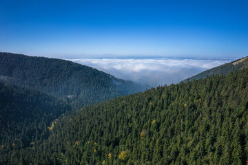 Aerial landscape of the green mountains in a daylight. Clouds low over the peaks, clear blue sky.