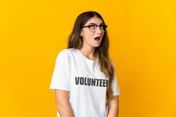 Young volunteer woman isolated on yellow background looking up and with surprised expression