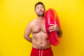 Middle age caucasian man holding inflatable donut isolated on yellow background and looking up