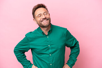 Middle age caucasian man isolated on pink background posing with arms at hip and smiling