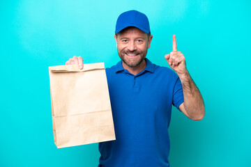 Middle age man taking a bag of takeaway food isolated on blue background pointing up a great idea