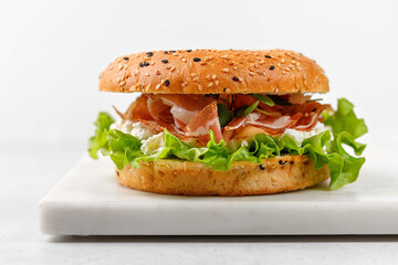 Delicious burger with prosciutto, cream cheese and lettuce for breakfast, sandwich, bagel with ham, close up
