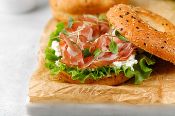 Sandwich with ricotta, prosciutto and microgreens, bagel with ham for breakfast on a paper.