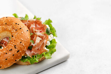 Sandwich with ricotta, prosciutto and microgreens, bagel with ham for breakfast on marble board. Space for text, close up.