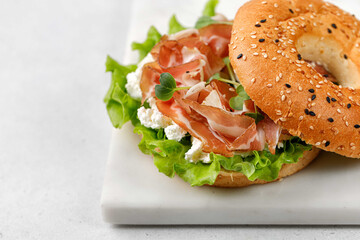 Sandwich with ricotta, prosciutto and microgreens, bagel with ham for breakfast on marble board. Space for text, close up.