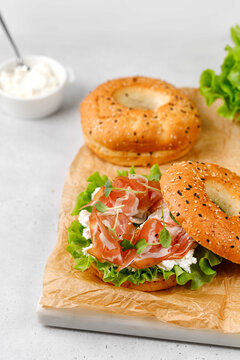 Bagels with ham prosciutto, cream cheese, letucce, microgreens on paper and grey background.