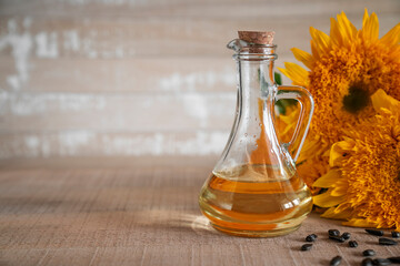 Obraz na płótnie Canvas Close-up sunflower oil in glass bottle with copy space. Sunflower oil in a glass bottle and sunflower seeds stand next yellow sunflowers on wooden background