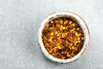 Chilli flakes in a bowl on a grey background, close up