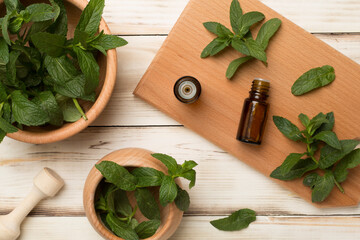 Melissa essential oil bottles with mortar pestle on wooden background, top view