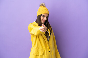 Young caucasian woman wearing a rainproof coat isolated on purple background making money gesture