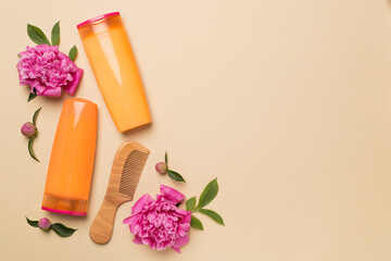 Shampoo and conditioner with peony flower and comb on color background, top view