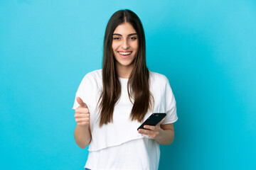 Young caucasian woman isolated on blue background using mobile phone while doing thumbs up