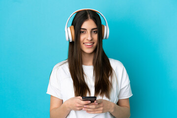 Young caucasian woman isolated on blue background listening music with a mobile and looking front