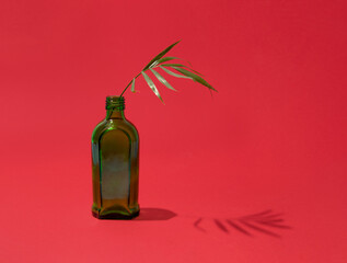 Single green bottle and palm branch, creative arrangement against rich red background. Summer...