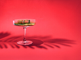 Champagne glass, golden drink and ice cubes, creative arrangement against red background. Summer sunset mood, relaxation, refreshment. 