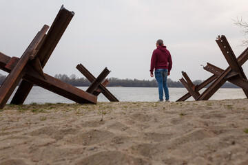 Ukrainian man among anti-tank czech hedgehogs on river bank. Stop Russian military agression, war...