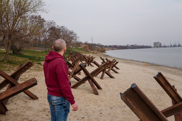 Ukrainian man on river bank among anti tank czech hedgehogs. War of Russia against Ukraine 2022. Protecting freedom from terrorism © elenaseiryk