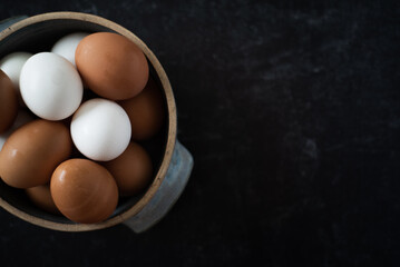 Top view of half a ceramic bowl of fresh organic brown and white eggs on dark background.