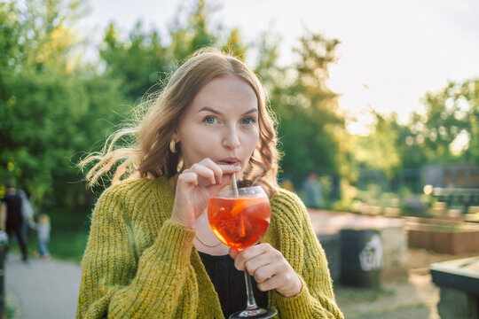 Closeup image of happy European 30s blonde woman having fun in cafe and drinking fruit cocktails with pleasure, outfit chilling in restaurant or street cafe