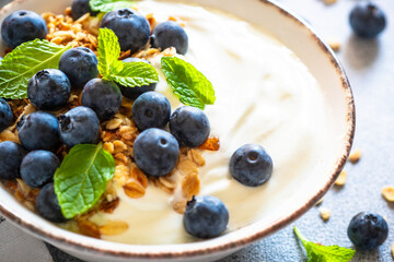 Greek Yogurt with granola and fresh bluebery at light stone table. Close up image.