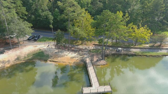 Aerial Footage Of A Silky Green Lake Along A Street With Cars Driving Surrounded By Lush Green Trees And Grass At Huddleston Pond Park In Peachtree City Georgia USA