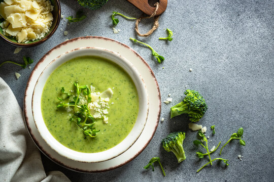 Green soup. Broccoli cream soup with parmesan and microgreen. Healthy vegan dish. Top view at stone table.