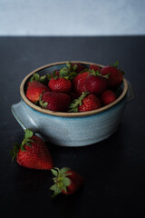 Bowl of raspberries spilling out in blue handmade ceramic bowl on dark background.