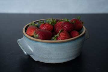 Bowl of raspberries in blue handmade ceramic bowl on dark background with grey concrete wall.