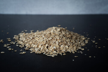 Closeup side top view of organic oats in a pile on dark moody background with concrete wall.