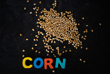 Top view of corn kernels with wooden colored letters spelling CORN on dark moody background.
