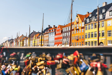 Romantic view on a summer sunny day at Nyhavn Pier with colorful beautiful buildings in the Old Town of Copenhagen, Denmark. Defocused foreground of castles on bridge. Perfect gift card. Copy Space - obrazy, fototapety, plakaty
