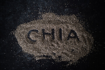 Top view of organic chia seeds in a pile on dark moody background word chia spelled in pile of oats.