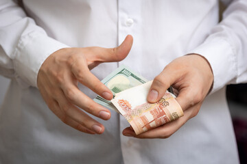 Cash rubles and dollars are counted close-up in the hands of a white man in a white shirt