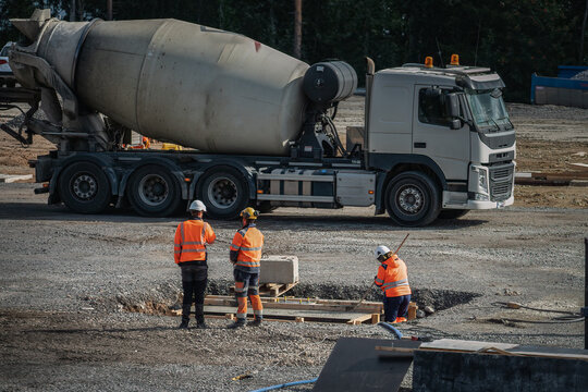 One unrecognizable female works and two unrecognizable male workers discusses problems at construction site, concrete transport truck at background