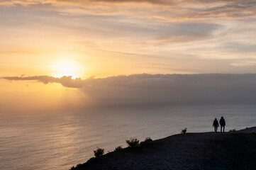 A couple of hikers walk on a cliff on the island of La Palma (Spain) at sunset