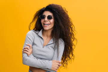 GOOD OFFER. Happy enjoyed pretty Latin female with afro in sunglasses crossing hands on chest, laughing, stay isolated over yellow background. Copy space, free place, fashion banner