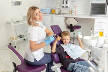 Dental clinic visit. Young positive woman dentist and small boy patient showing thumbs up sign in dentist office