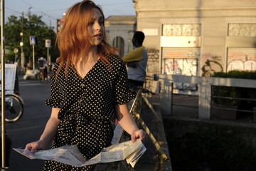 Fototapeta na wymiar Beautiful girl, tourist in Milan watching map. Canals district. Sunset light. European city.