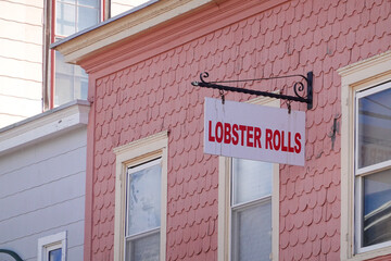 Obraz premium A white sign that says Lobster Rolls in red letters hanging from a house with pink wooden shingles