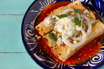 Fried potato tacos called flautas with red sauce and cheese. Mexican food