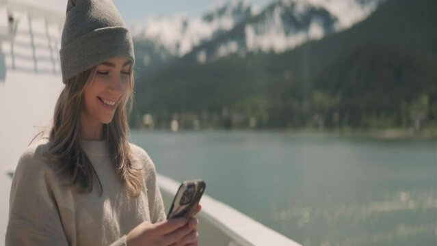 Blonde woman wearing a beenie takes pictures outside on a cruiseship traveling through Alaska. Medium Shot. Anamorphic 