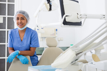 Confident professional dentist woman posing in dental clinic, looking with smile at camera