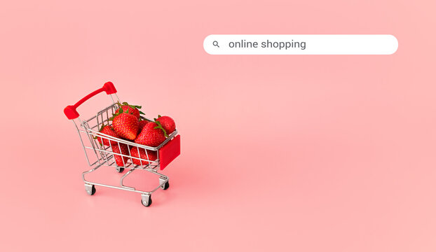 Fresh red strawberry in shopping card on pink background with search box. Online shopping and Valentines Day minimalistic concept. Black Fridays sales banner. Healthy, organic, vegan food. 